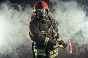 Eine Person mit Schutzkleidung und Atemschutzmaske geht durch eine Rauchwolke.